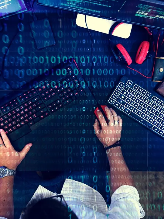 Scrivania vista dall’alto con computer, tastiere e codice binario