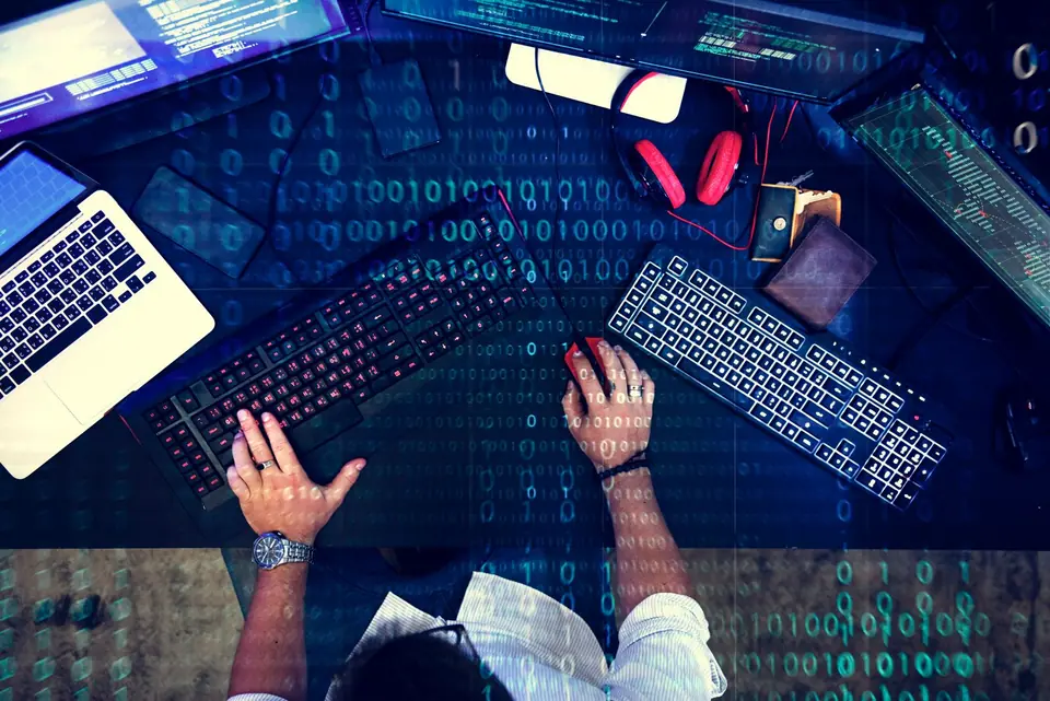 Scrivania vista dall’alto con computer, tastiere e codice binario